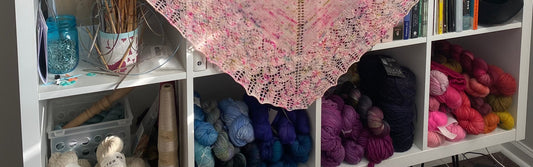 beautifully arranged yarn stash in blues, purples, and reds, along with books and knitting needles in an open faced Ikea cubby shelf