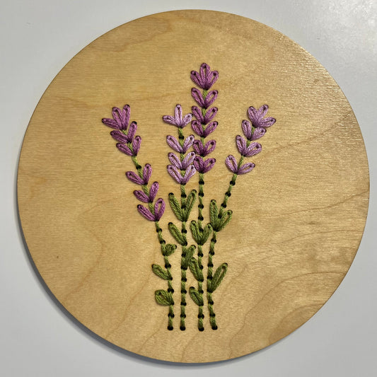A completed embroidery kit depicting a bouquet of flowers arranged on a round wooden disk.