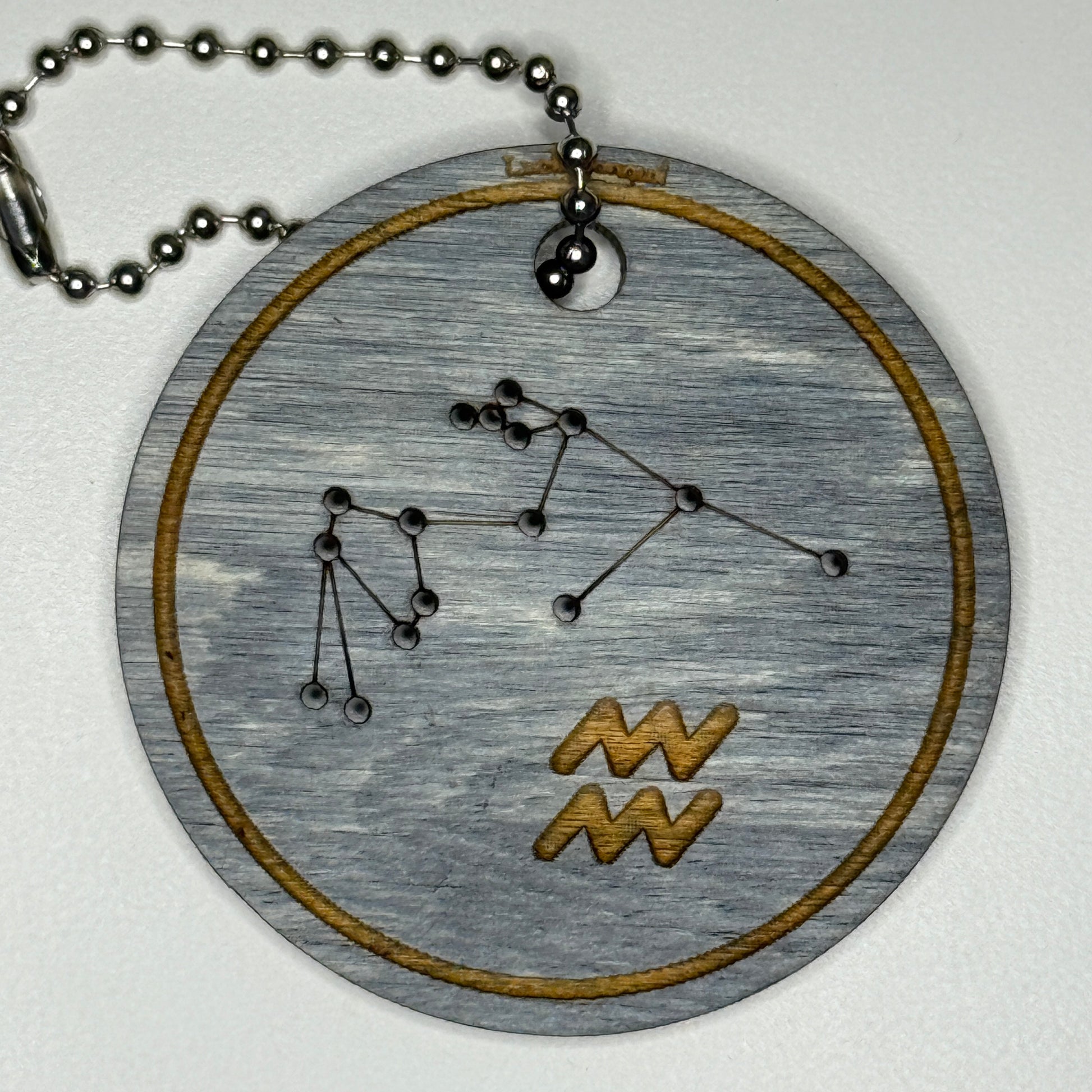 Circular pendant with astrological symbol & stars on a blue wood, set against a white background