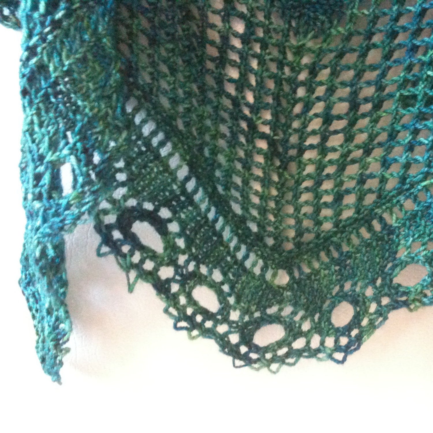 Closeup of a teal green lace shawl against a white background.