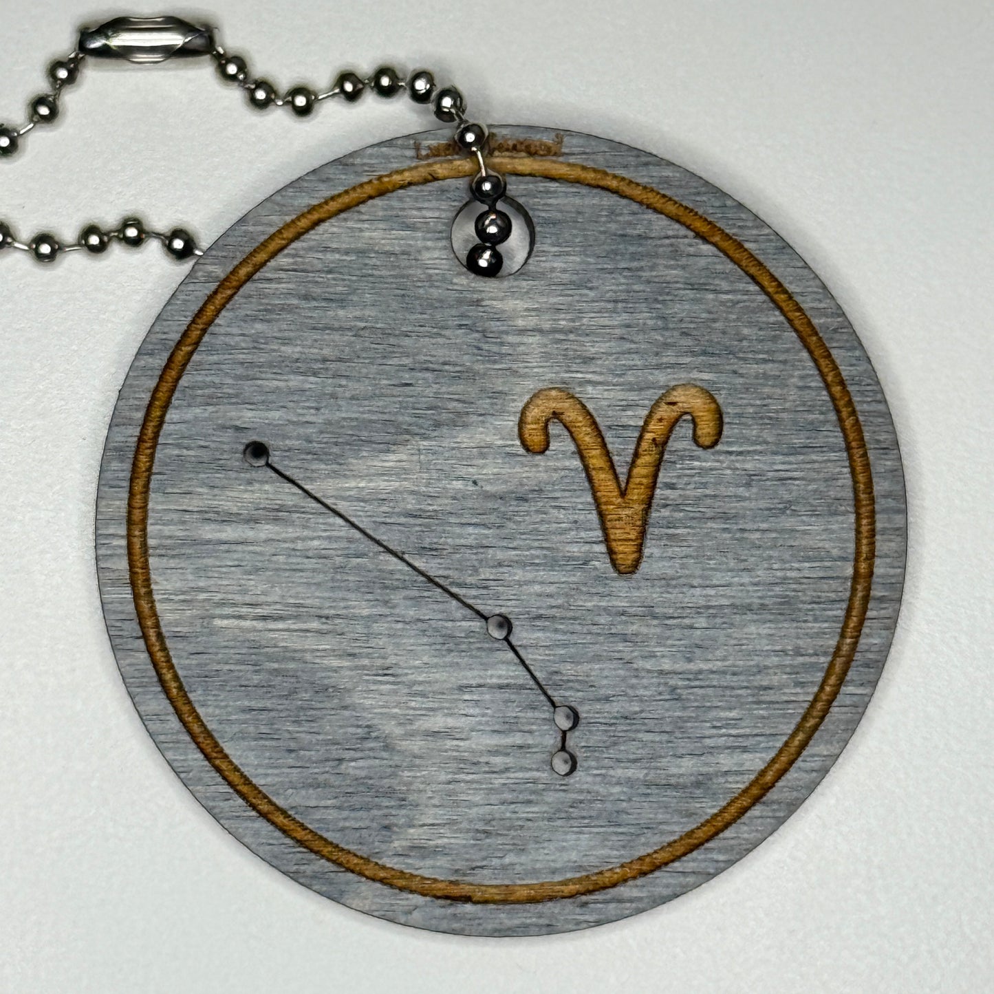 Circular pendant with astrological symbol & stars on a blue wood, set against a white background