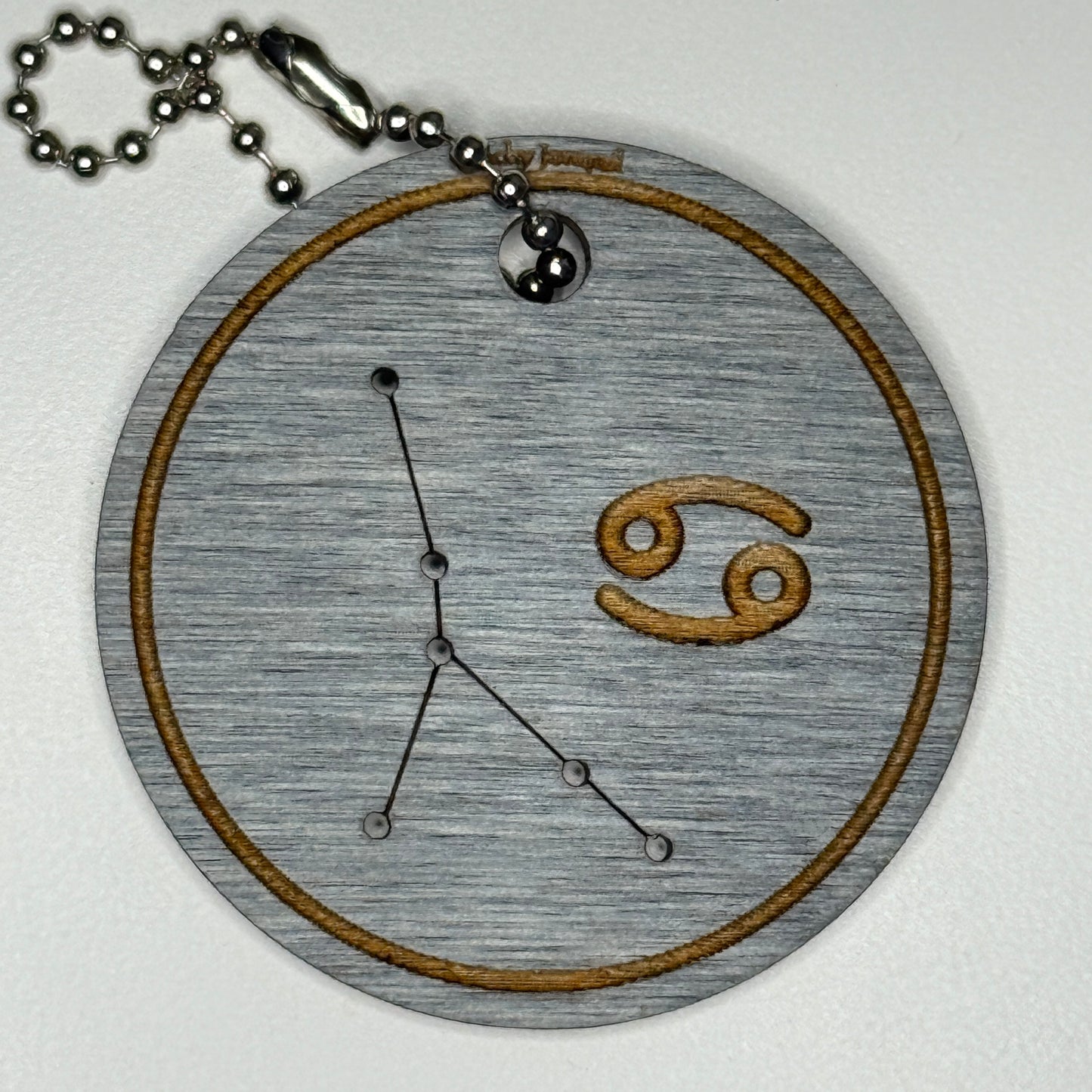 Circular pendant with astrological symbol & stars on a blue wood, set against a white background