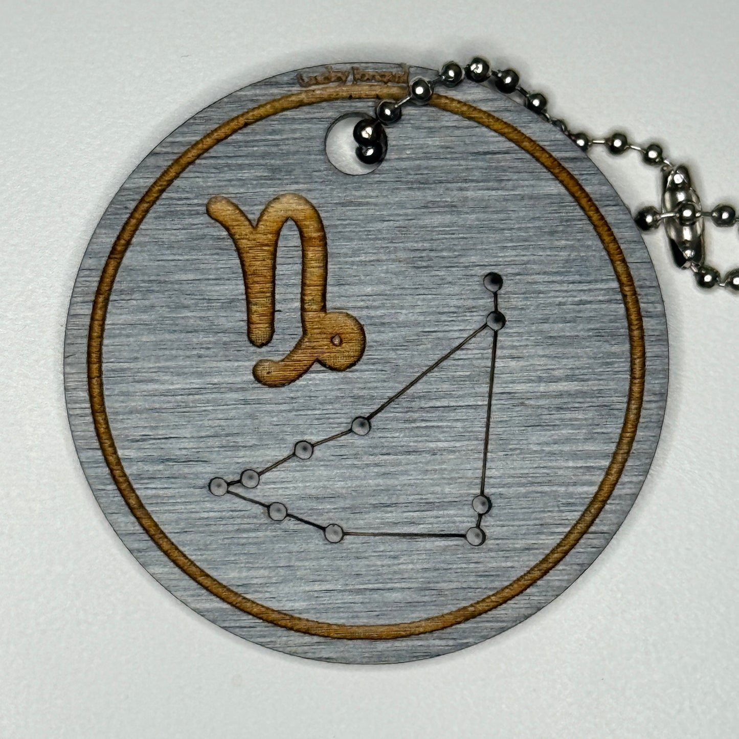 Circular pendant with astrological symbol & stars on a blue wood, set against a white background