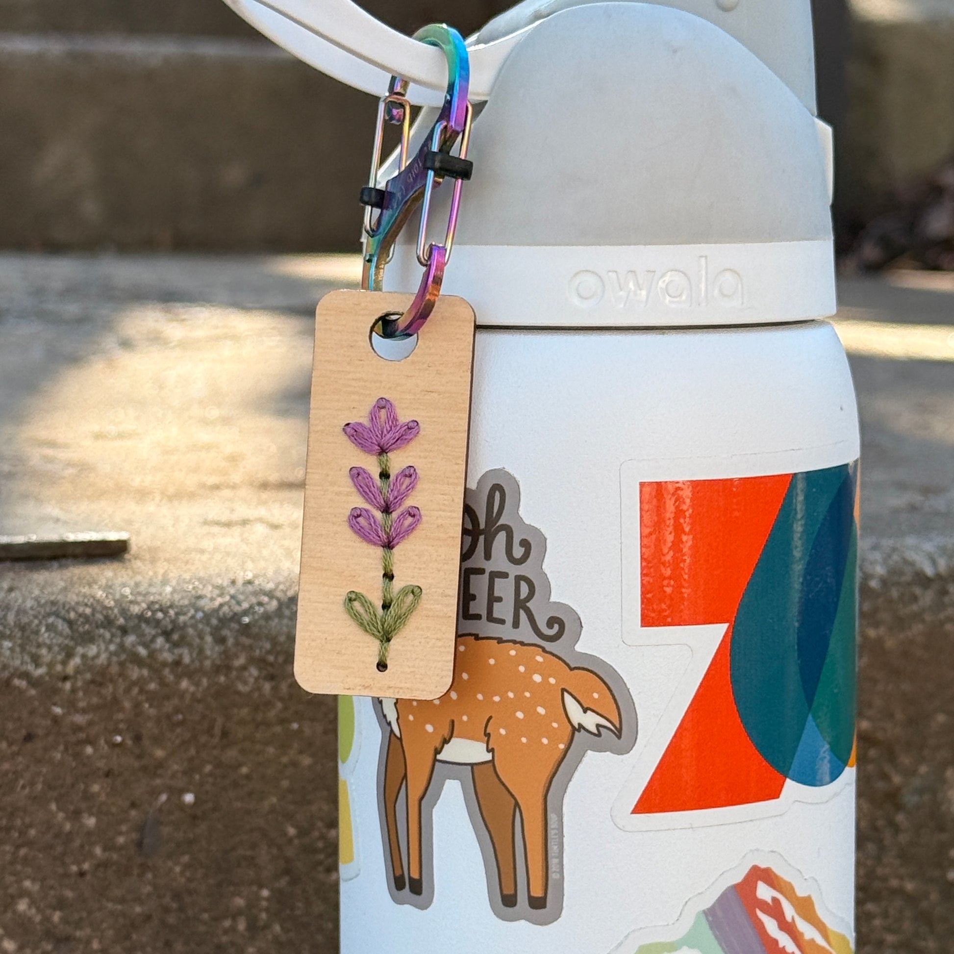sticker white water bottle closeup with a rainbow careener attaching a wooden tag stitched with a lavender sprig 