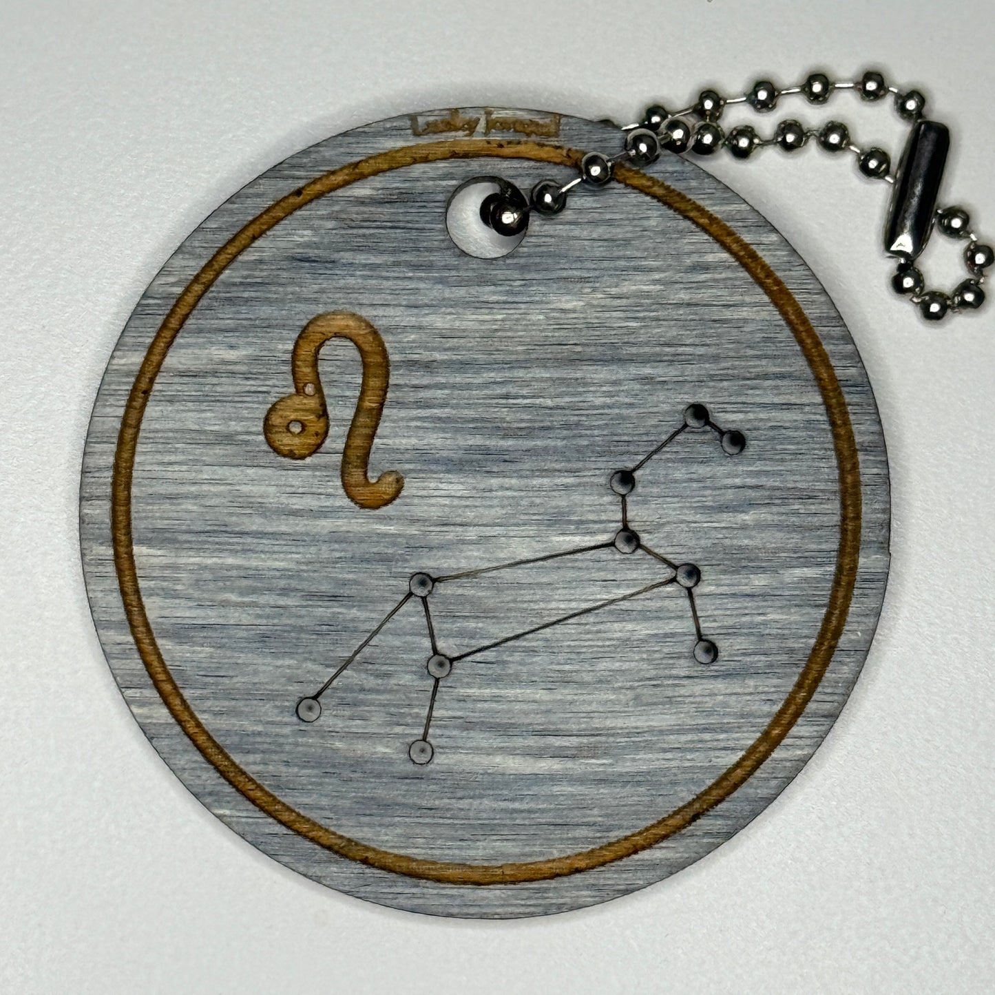 Circular pendant with astrological symbol & stars on a blue wood, set against a white background