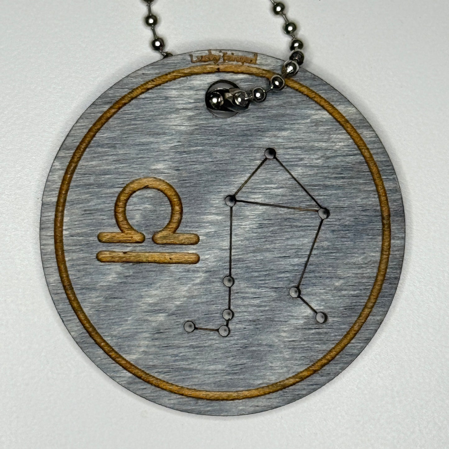 Circular pendant with astrological symbol & stars on a blue wood, set against a white background