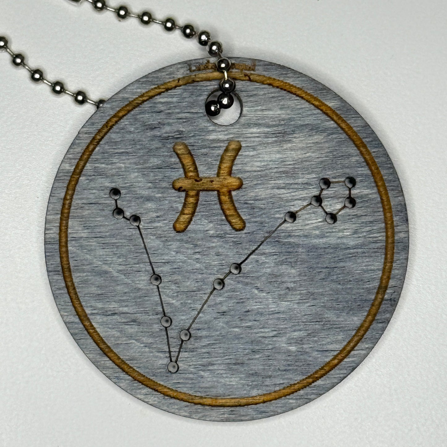 Circular pendant with astrological symbol & stars on a blue wood, set against a white background
