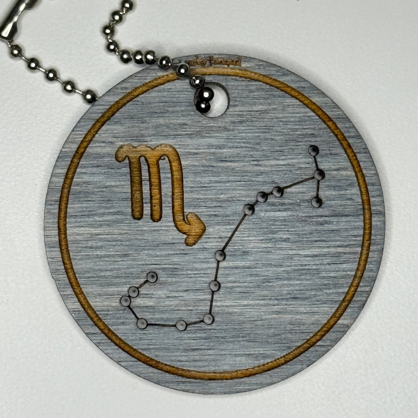 Circular pendant with astrological symbol & stars on a blue wood, set against a white background