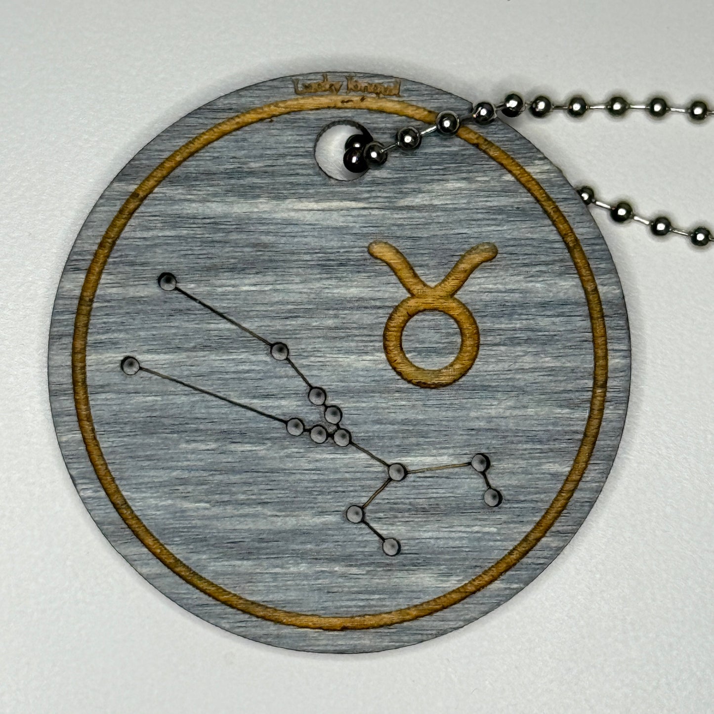 Circular pendant with astrological symbol & stars on a blue wood, set against a white background