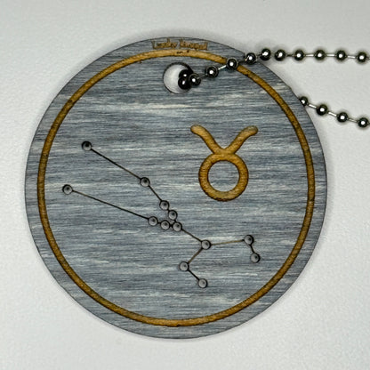 Circular pendant with astrological symbol & stars on a blue wood, set against a white background