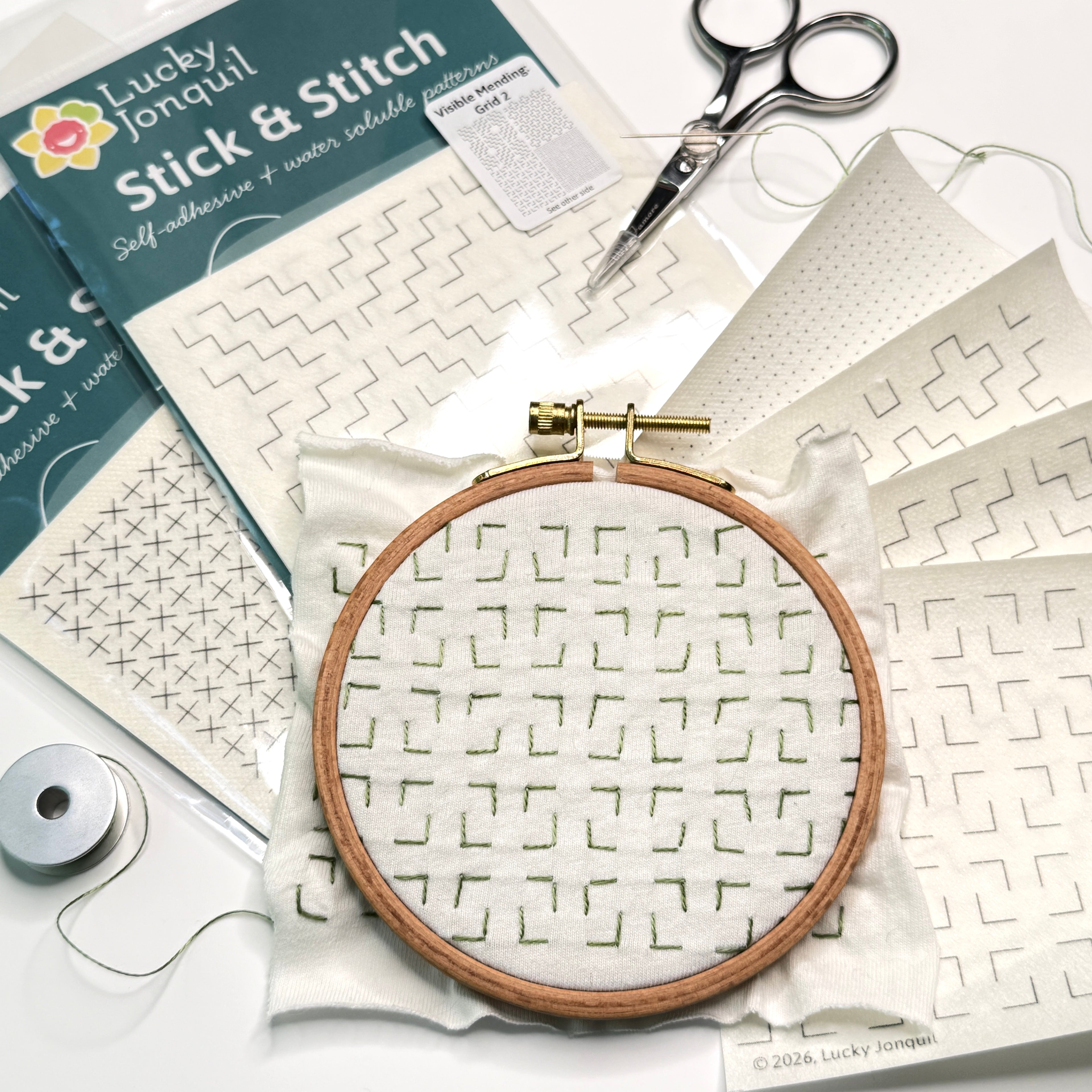 Embroidery hoop with patterned fabric, scissors, thread, and Lucky Jonquil visible mending packs on a white background