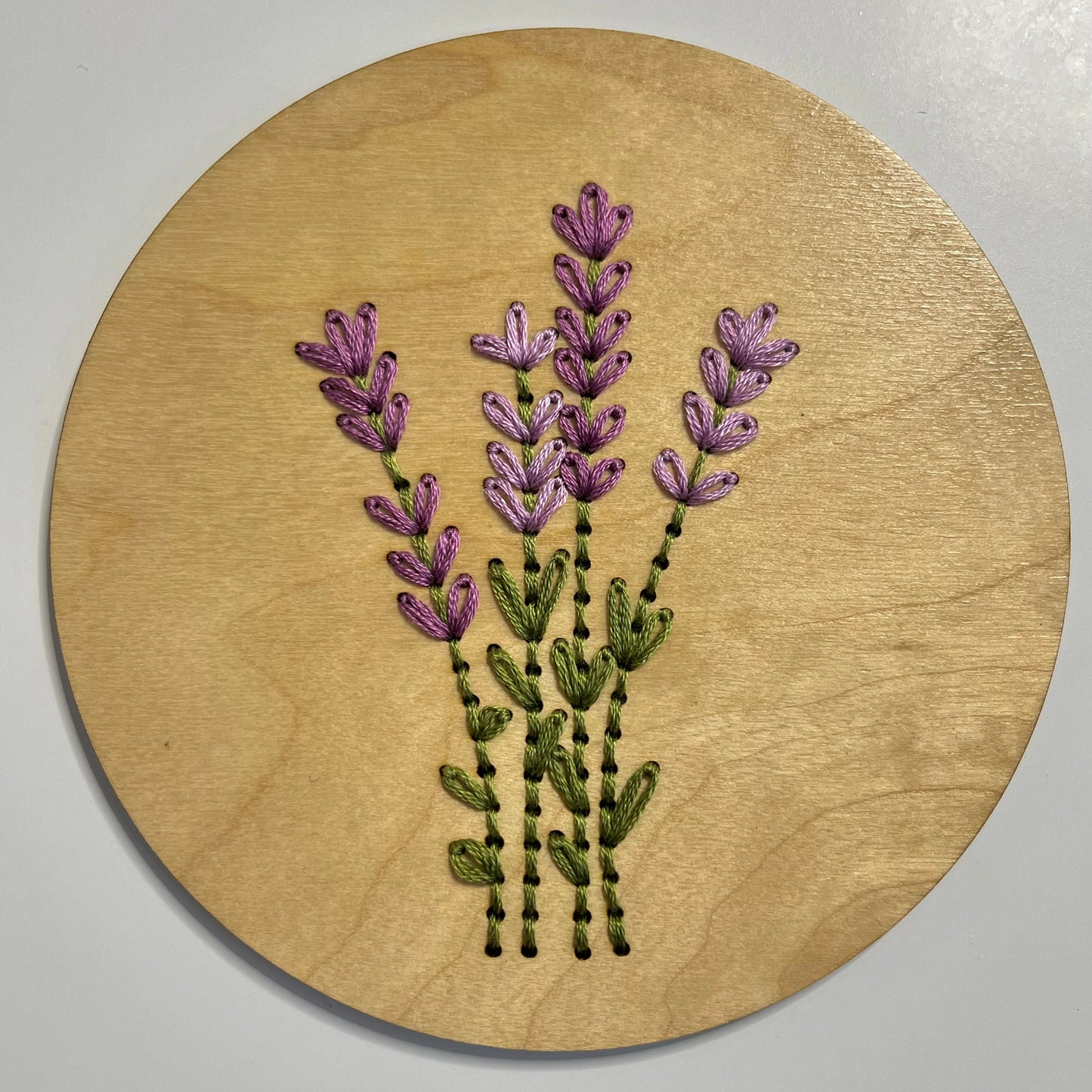 A completed embroidery kit depicting a bouquet of flowers arranged on a round wooden disk.