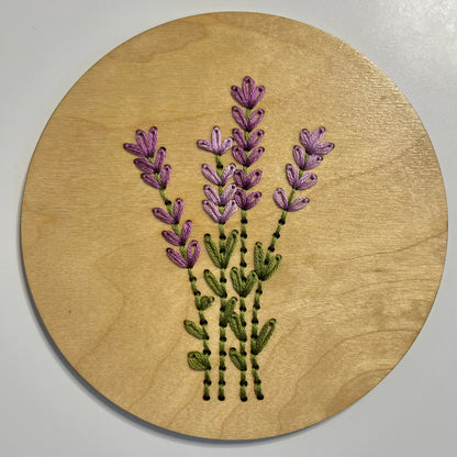 A completed embroidery kit depicting a bouquet of flowers arranged on a round wooden disk.